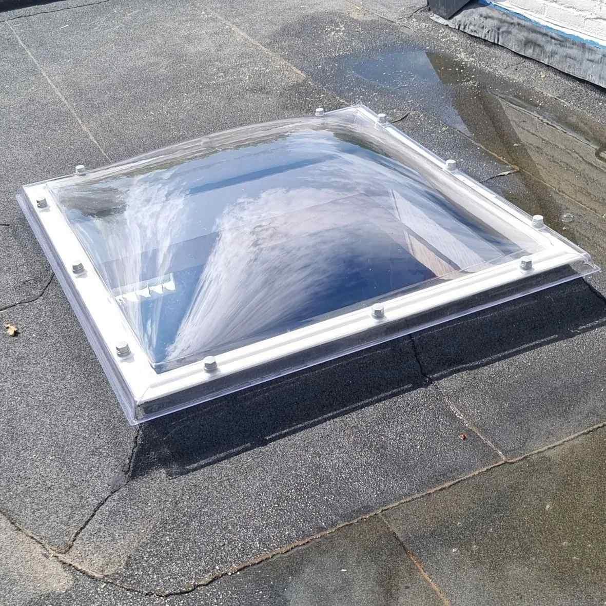 Vierkante heldere lichtkoepel op een witte opstand op een bitumen plat dak