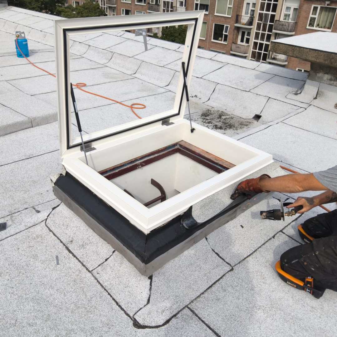 Monteur bezig met het waterdicht afwerken van een dakluik op bestaande opstand op plat dak